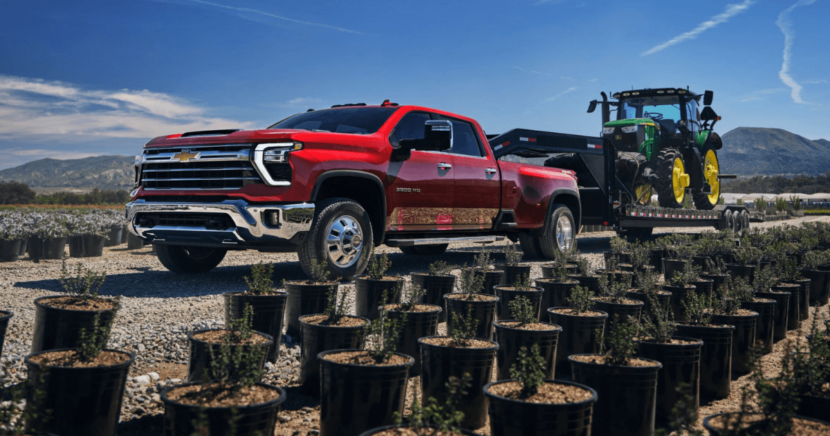 A red 2025 Chevy Silverado 2500 driving through a plant nursery while hauling a tractor