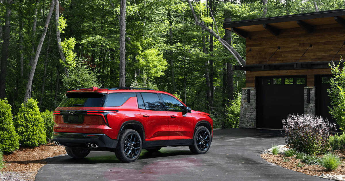 A red Chevrolet Traverse parked in the driveway of a cabin in the woods