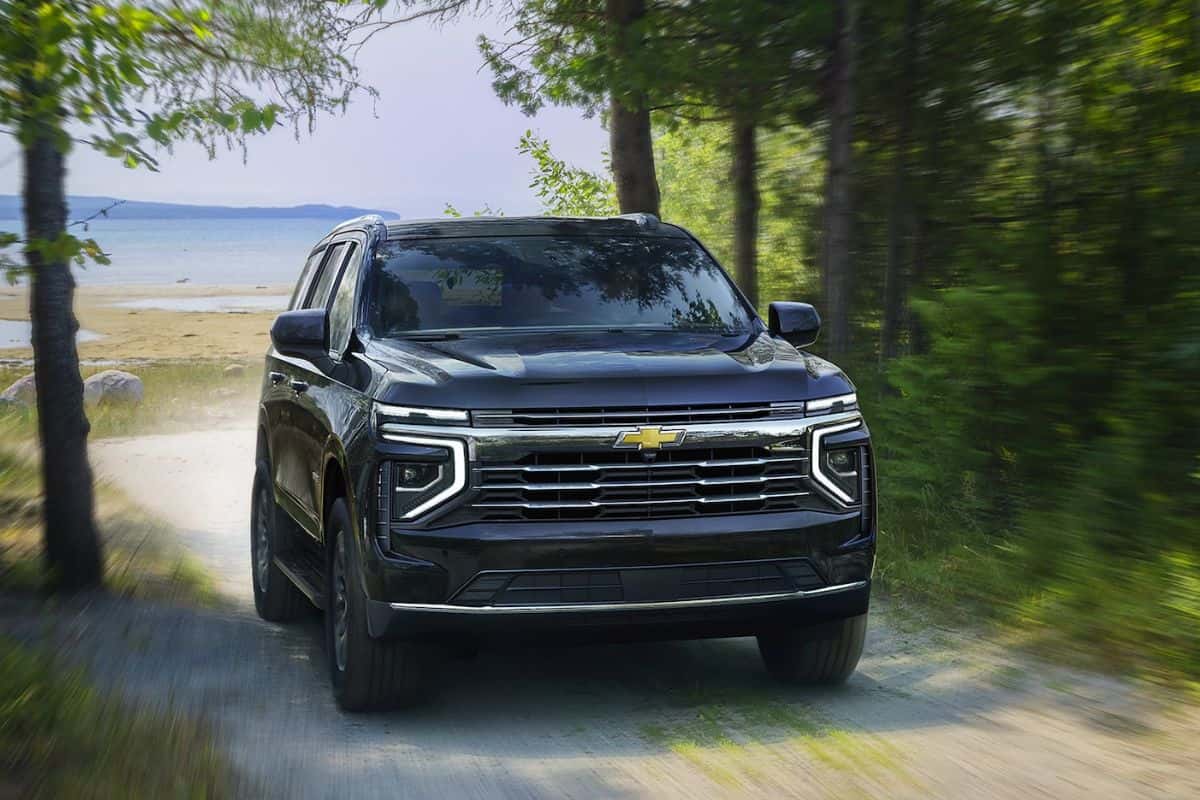 A blue Chevrolet Tahoe driving down a dirt road from a beach through a forest