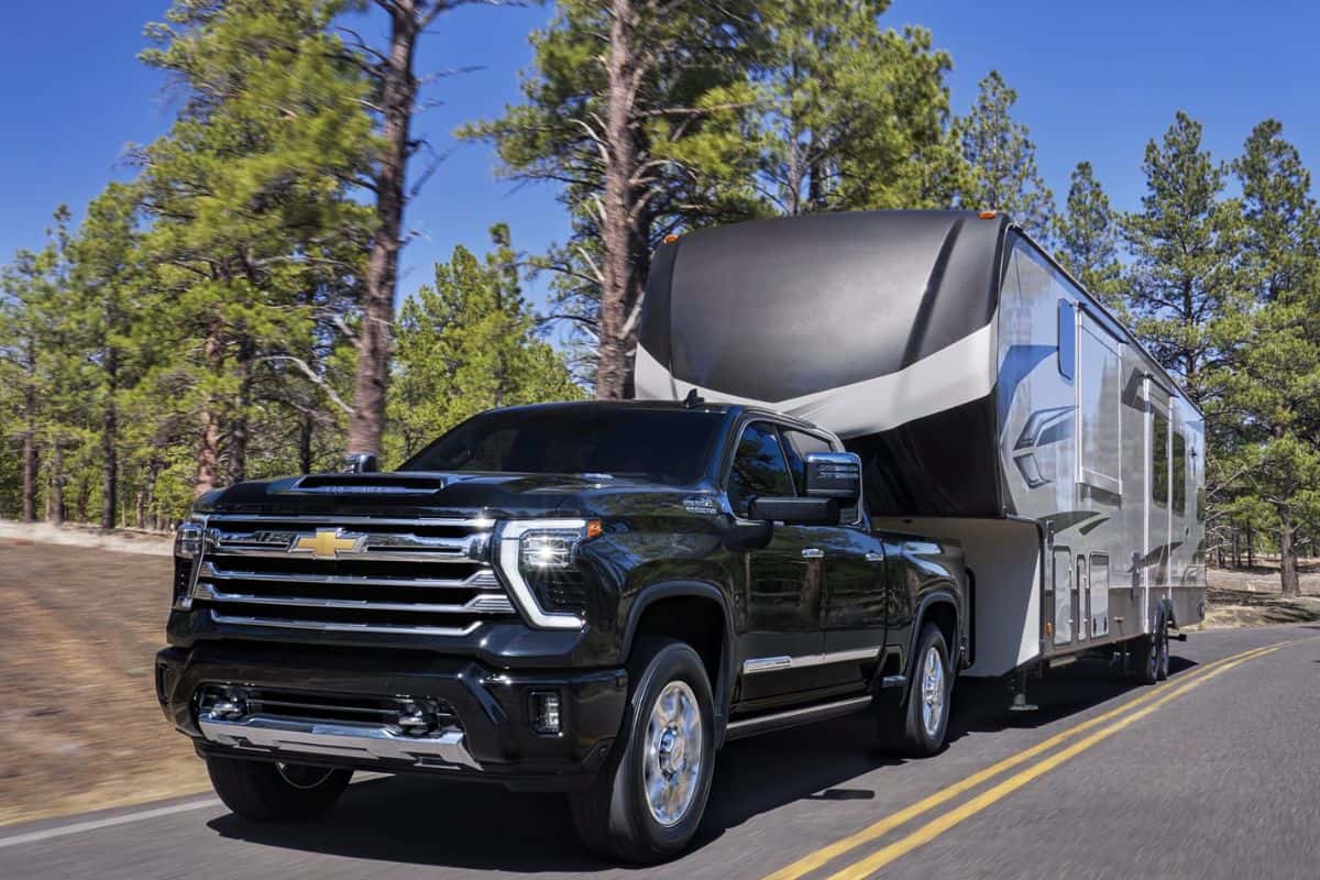 A black Chevy Silverado HD towing a trailer on the road, driving through a forest