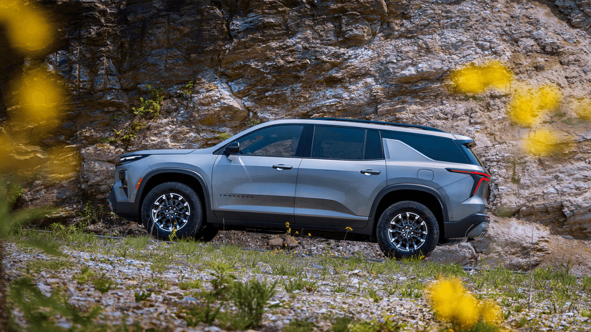 A light gray Chevy Traverse traveling off-road up a hill