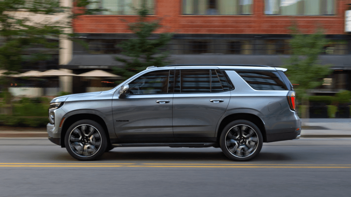 A silver Chevy Tahoe in profile driving down the road in a town