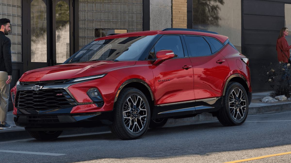 A red Chevy Blazer parallel parked by the sidewalk as a man walks by