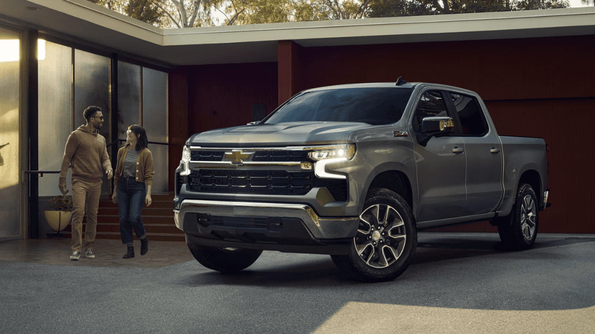 A grey Chevrolet Silverado 1500 parked in a driveway as a couple approaches it