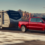 A red Chevrolet Silverado 1500 towing a Cougar trailer wheel driving through a desert