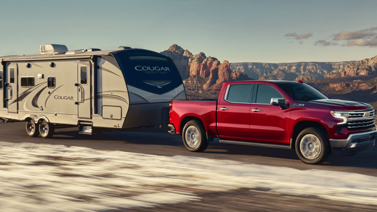 A red Chevrolet Silverado 1500 towing a Cougar trailer wheel driving through a desert