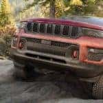 A red 2022 Jeep Grand Cherokee Trailhawk is shown from the front while climbing over a rock after leaving a Jeep dealer in Williston.