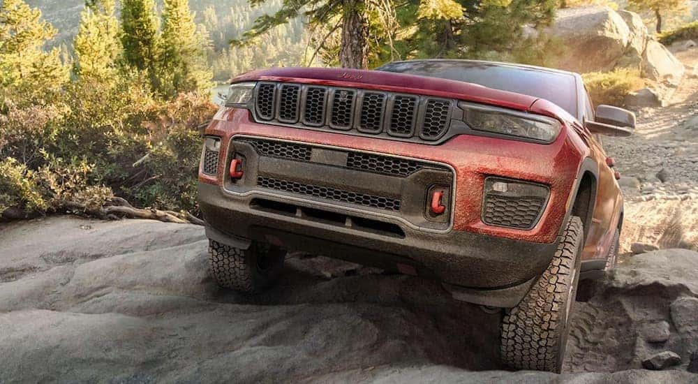 A red 2022 Jeep Grand Cherokee Trailhawk is shown from the front while climbing over a rock after leaving a Jeep dealer in Williston.