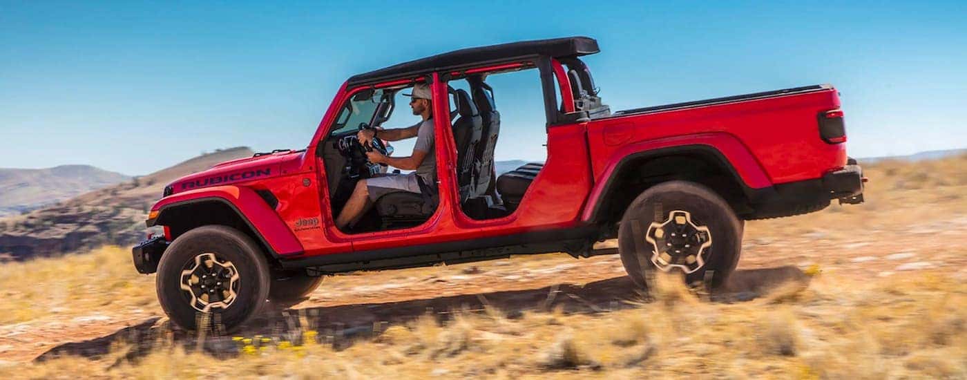 A red 2021 Jeep Gladiator with no doors is shown from the side driving on a trail.