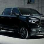 A black 2021 Ram 1500 is shown from the side parked in front of a cement building.