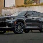 A grey 2022 Jeep Grand Cherokee L is shown parked in a driveway next to a concrete wall.