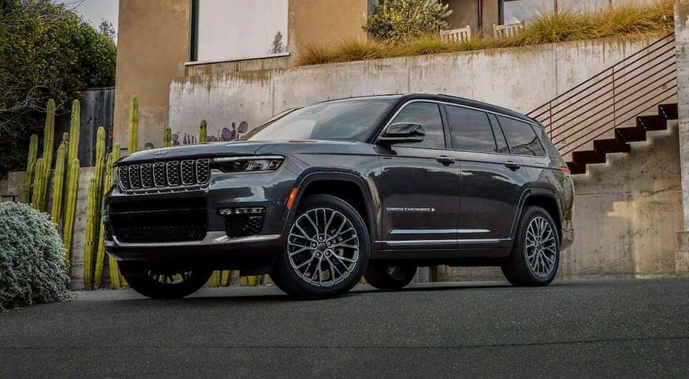 A grey 2022 Jeep Grand Cherokee L is shown parked in a driveway next to a concrete wall.