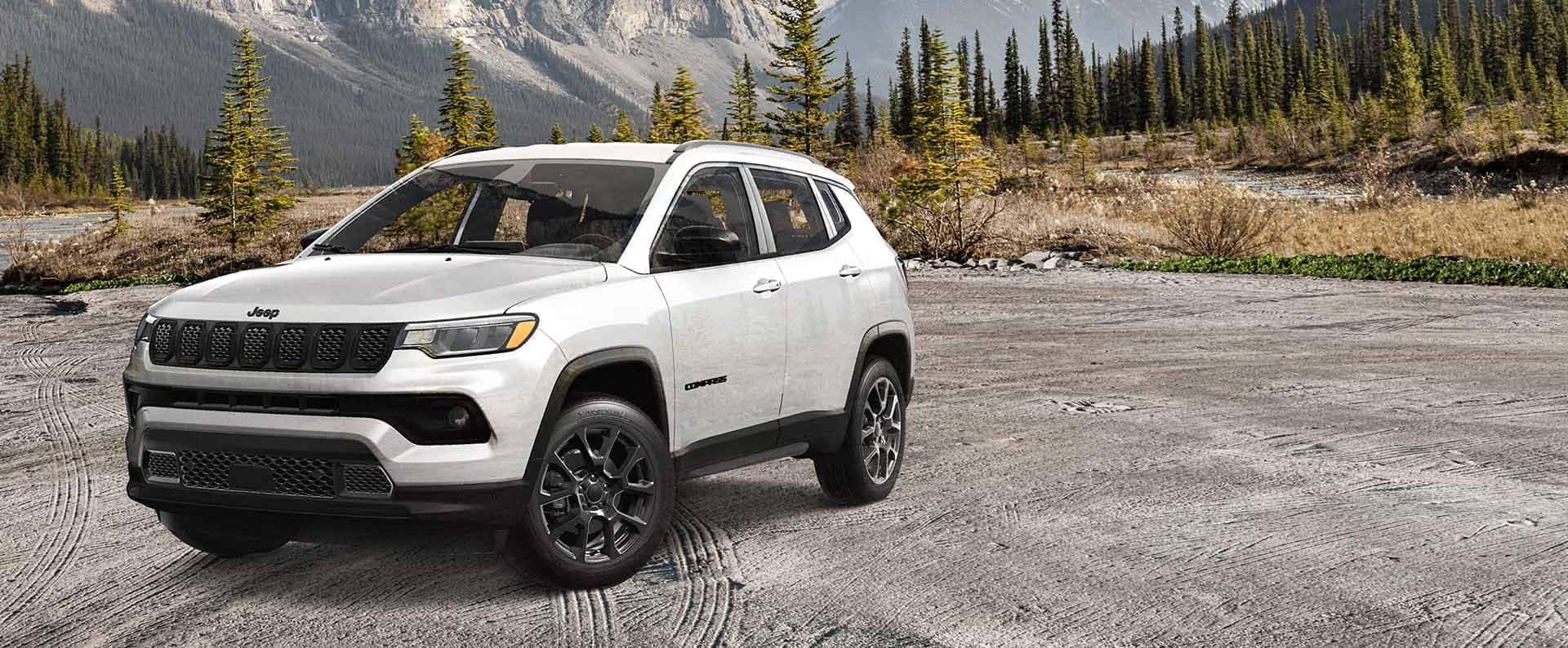 A white 2025 Jeep Compass parked in a clearing near a forest
