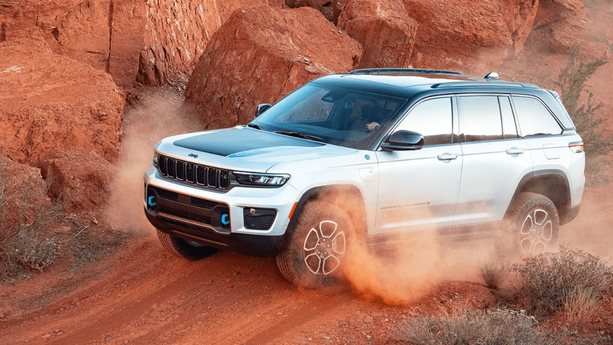 A silver Jeep Grand Cherokee kicking up dust as it drives off-road through a rocky desert