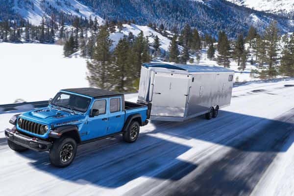 A blue Jeep Gladiator driving on a snowy road while towing a trailer