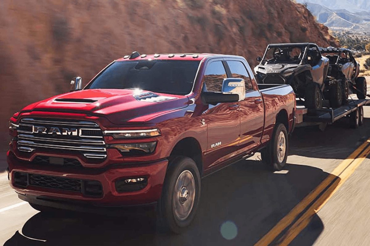 A red RAM 2500 towing a flatbed with a dune buggy on it