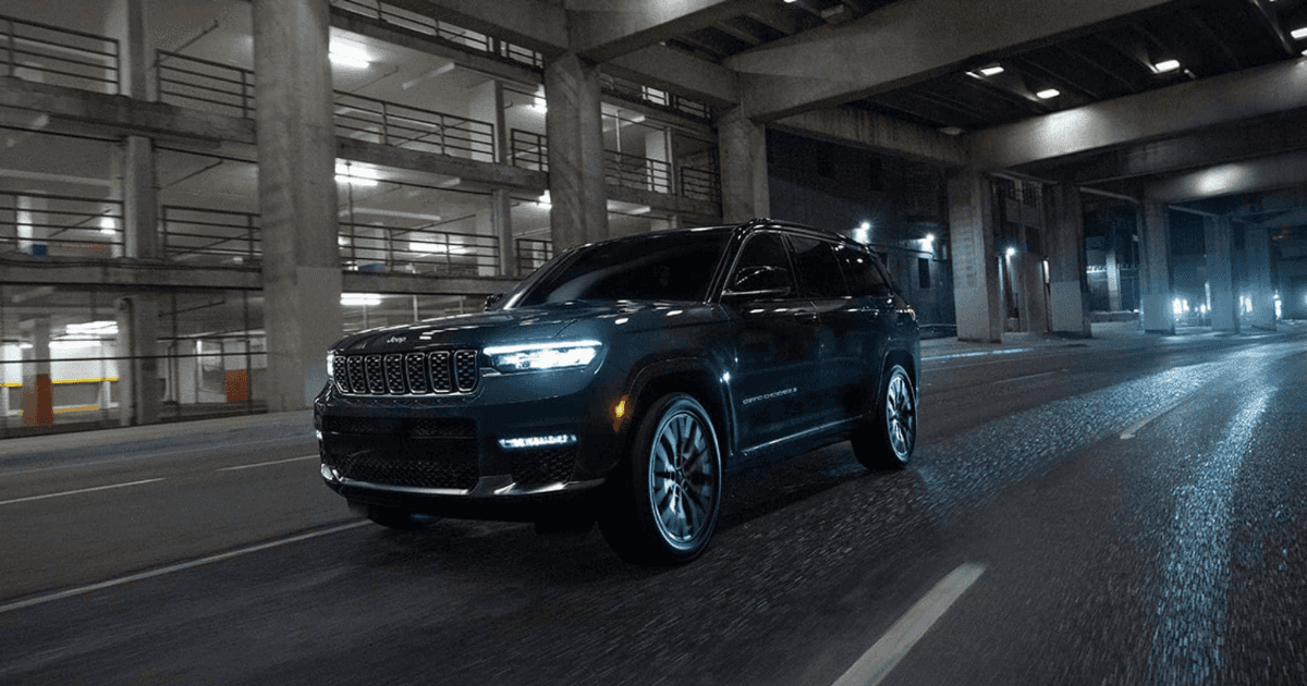A black Jeep Grand Cherokee driving at night by a parking garage