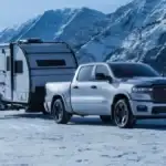 A silver RAM 1500 on top of a snowy hill towing a trailer