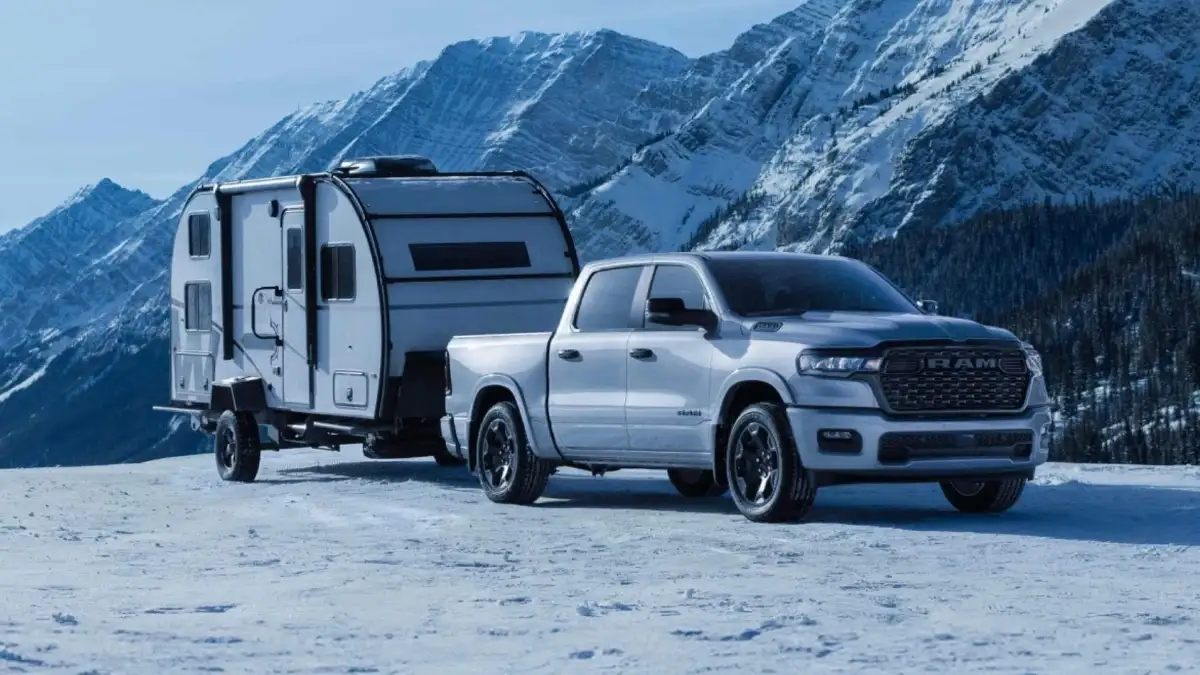 A silver RAM 1500 on top of a snowy hill towing a trailer