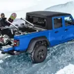 A blue Jeep Gladiator in the snow with two men unloading snowboards