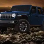 A blue Jeep Wrangler driving over rocky terrain