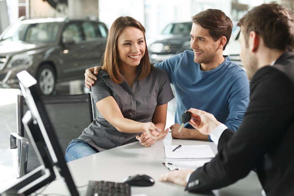 A dealership team member giving keys to two people sitting at a desk