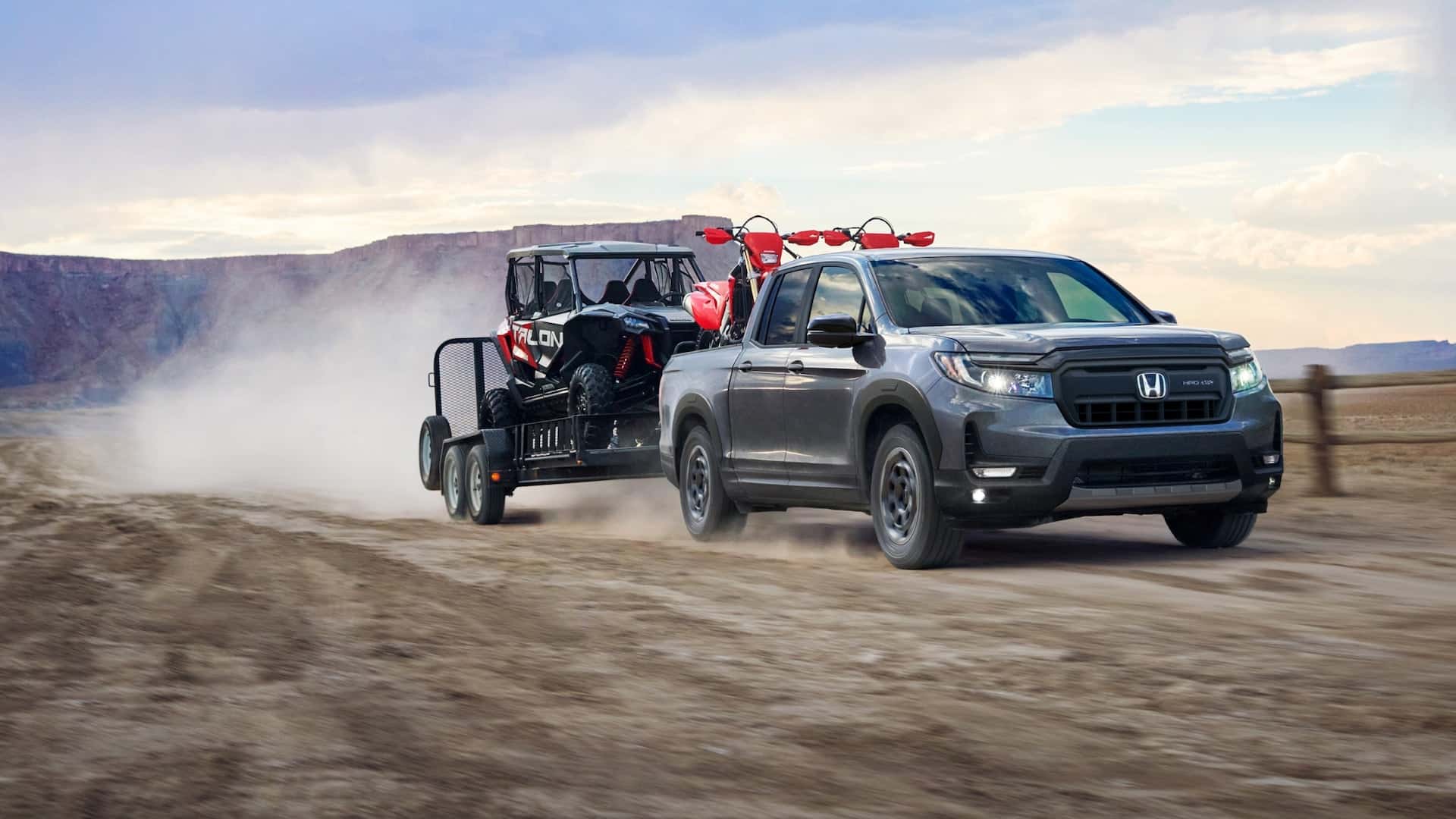 A dark gray 2025 Honda Ridgeline hauling a flatbed with a cart through a desert