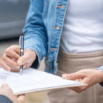 A woman signing a document handed to her by a car salesman at a dealership