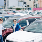 A saleswoman showing off a car on a dealership lot to a customer