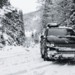 A black SUV driving down a snow-covered road in a forest