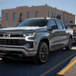 A gray Chevy Silverado hauling a vintage red car through a town