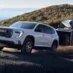 A white GMC Acadia hauling a trailer on a dirt road