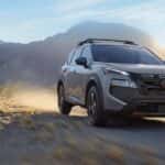 A silver Nissan Rogue driving over a dirt road in a desert