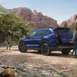 A blue Honda CR-V parked at a campsite with a person opening the trunk with the automatic tailgate