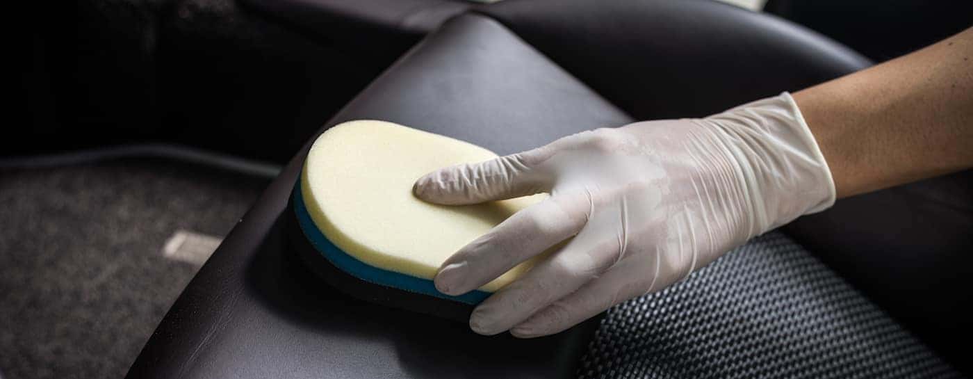 Hand in a rubber glove using a yellow sponge to clean leather seats in a vehicle