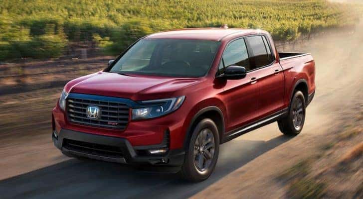 A red 2022 Honda Ridgeline Sport is shown from the front at an angle while it drives down a dirt road after leaving a Honda dealer.