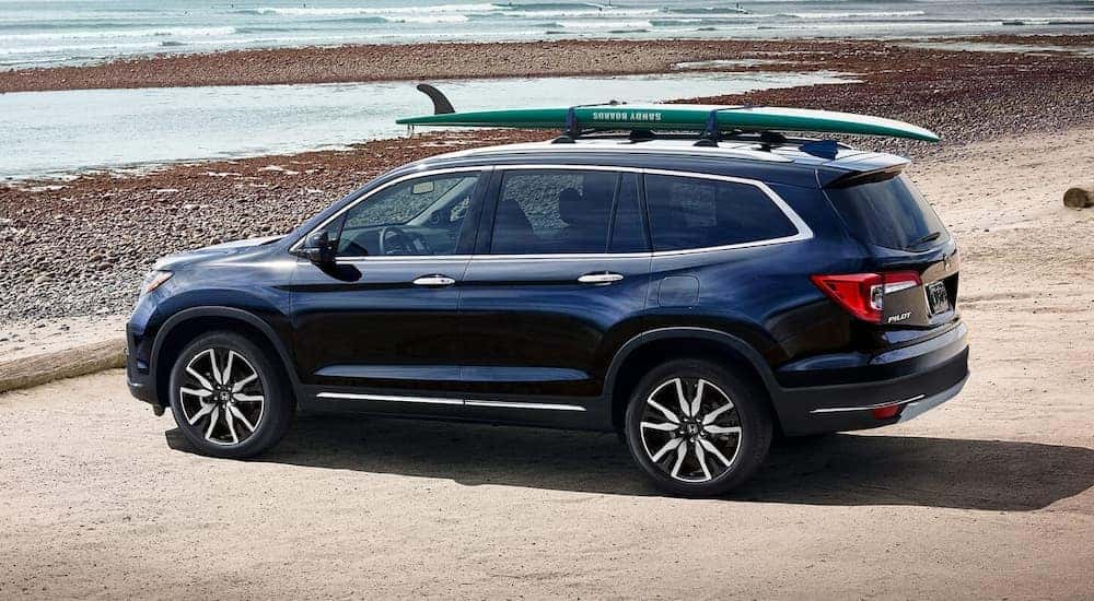 Dark blue Honda Pilot with a surfboard on the roof parked on the beach