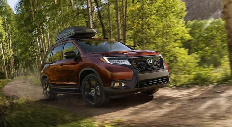A brown 2022 Honda Passport is shown from the front at an angle while driving through the forest.