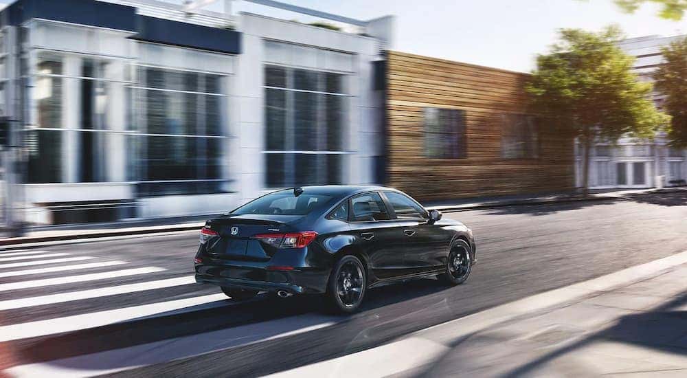 A black 2023 Honda Civic Sport is shown driving through a town center.