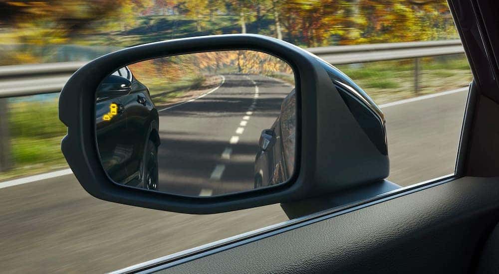 A close up shows the blind spot monitoring icon on the mirror of a blue 2023 Honda CR-V.