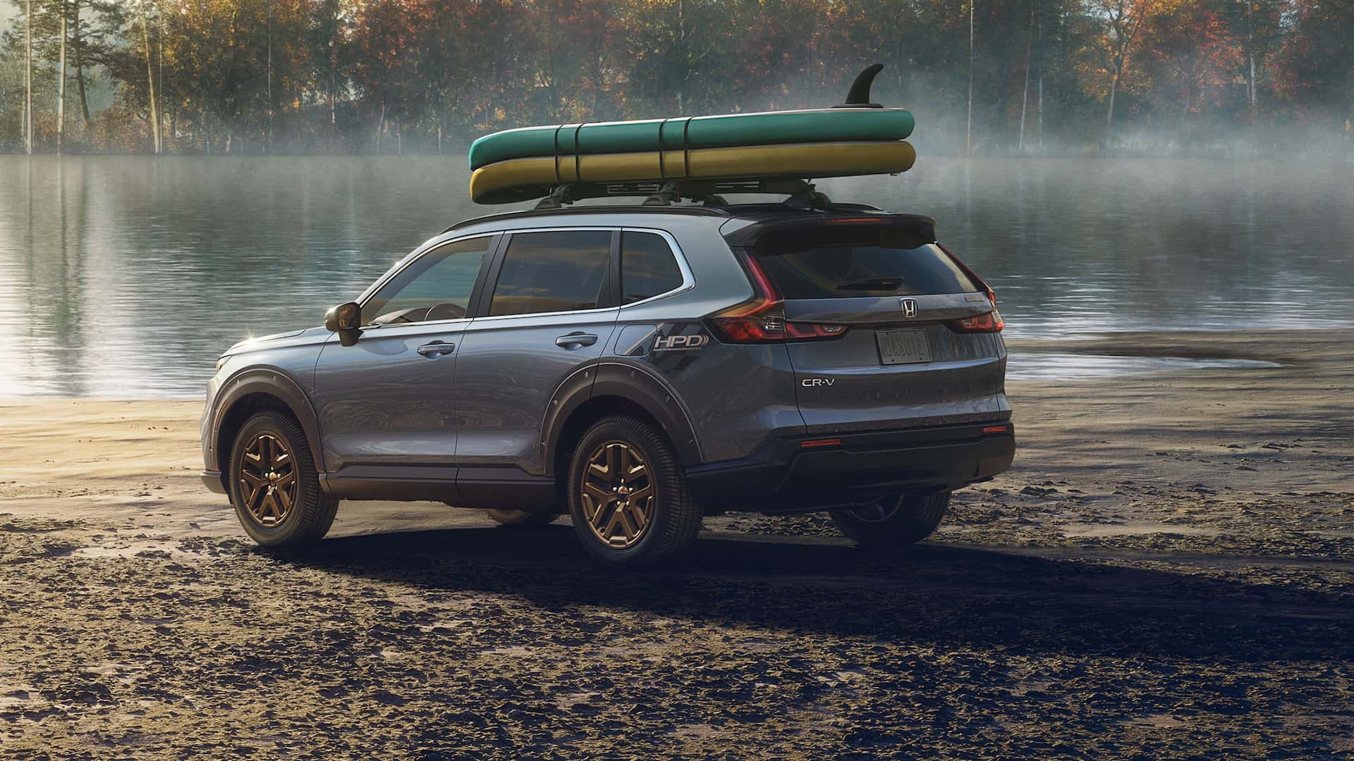A gray Honda CR-V parked at a lake bed with surfboards strapped to its roof
