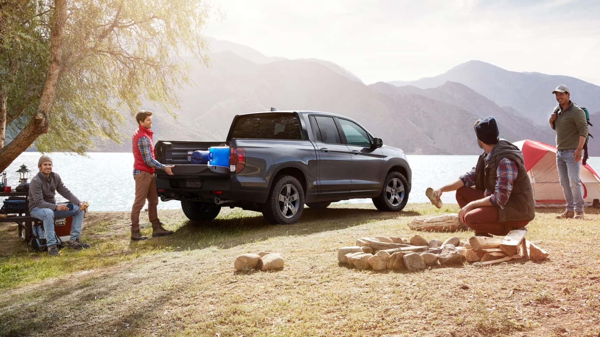 A grey Honda Ridgeline at a camp site with a group of men