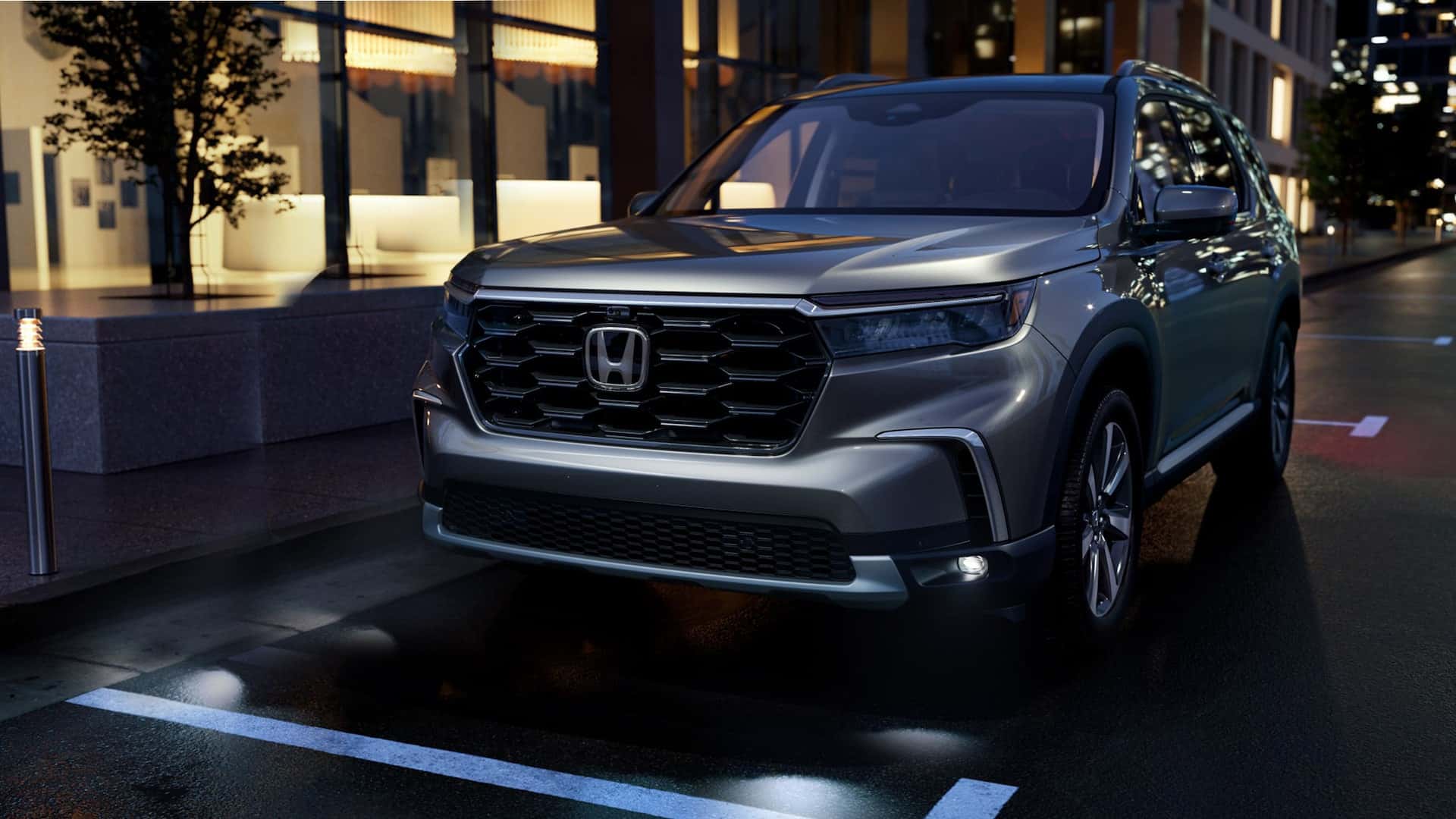 A gray Honda Pilot parallel parked in a city at night
