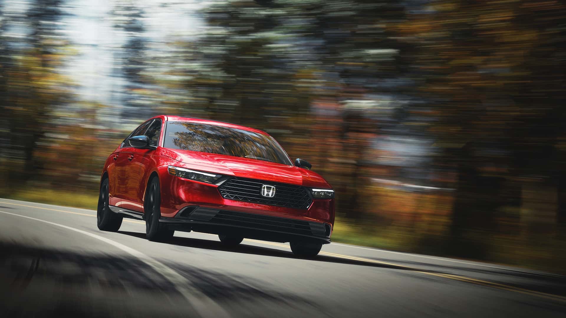 A red Honda Accord quickly driving down the road by a forest
