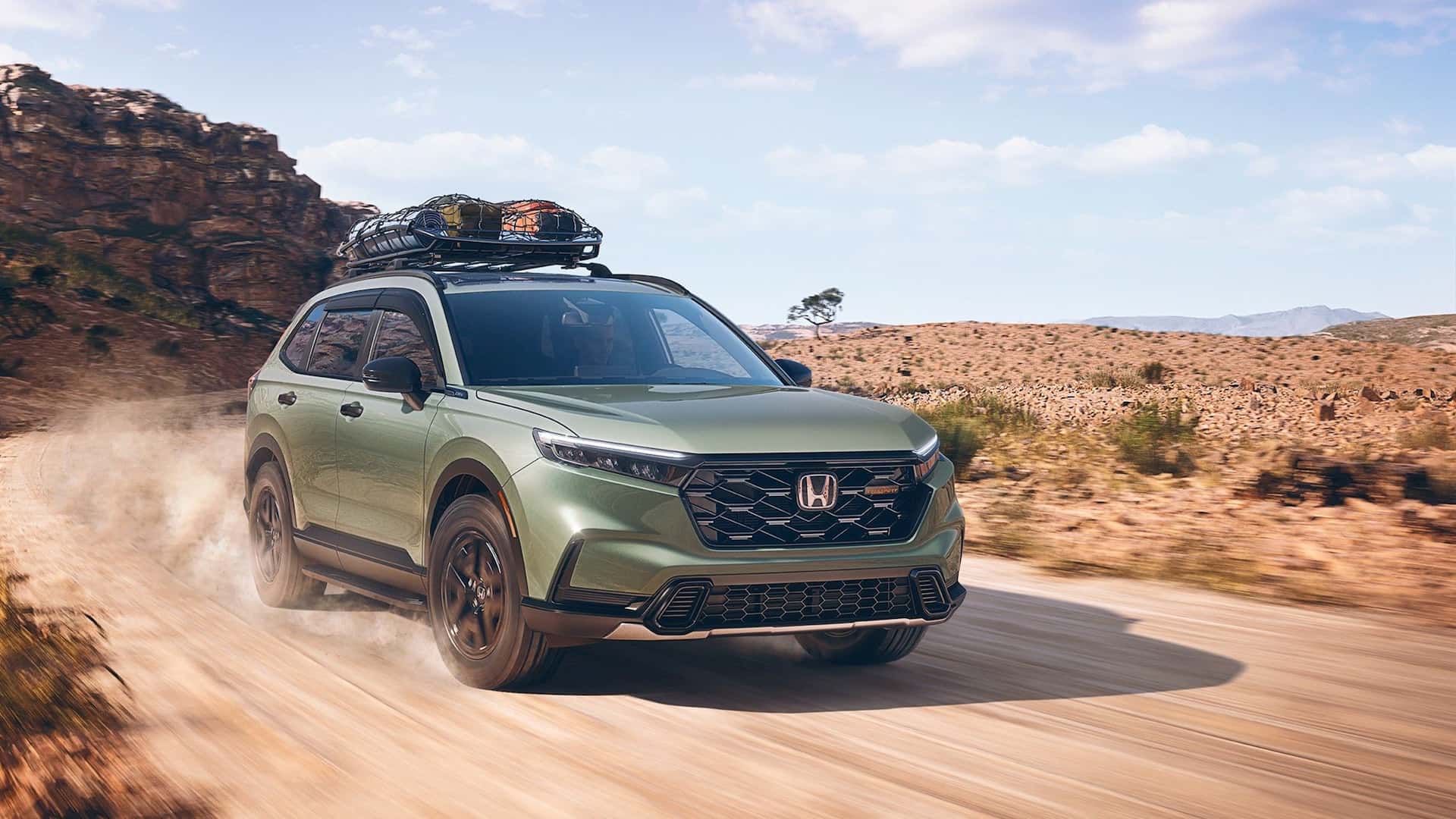 A green Honda CR-V kicking up dirt as it drives down a trail in a desert