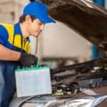 A technician in blue and yellow replacing a vehicle's battery