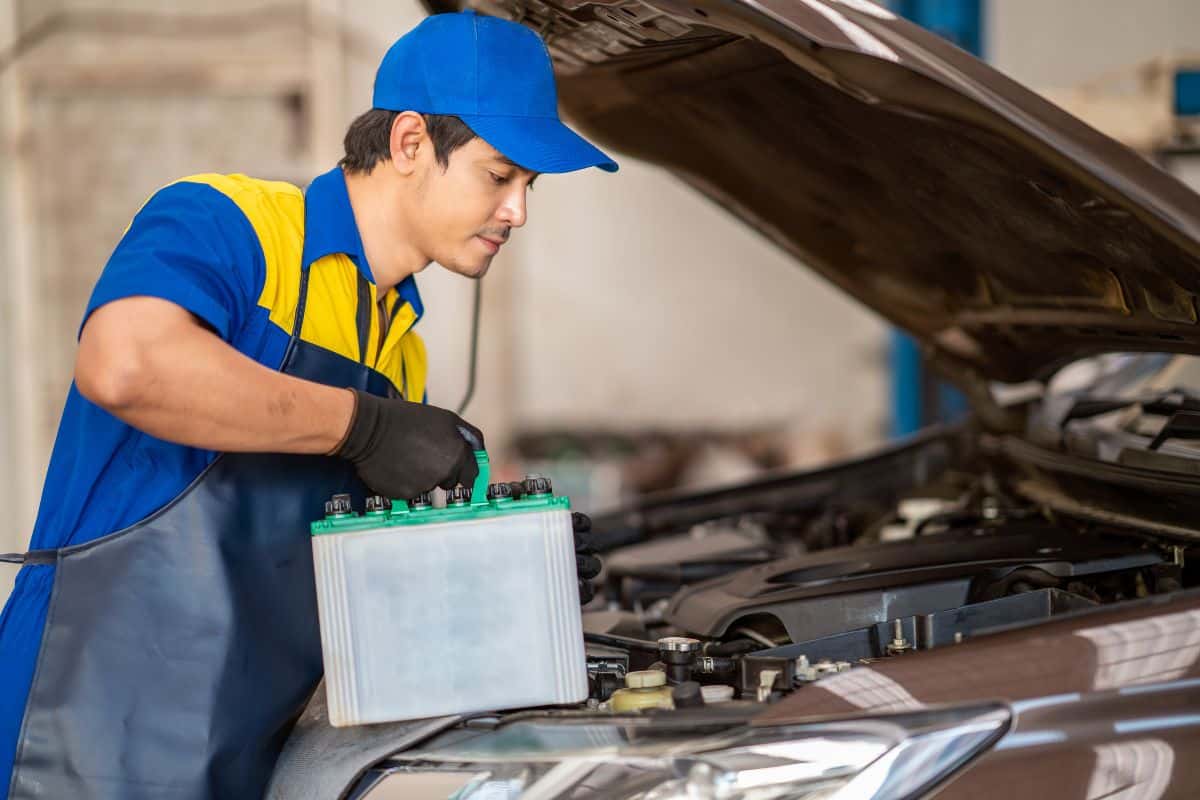 A technician in blue and yellow replacing a vehicle's battery