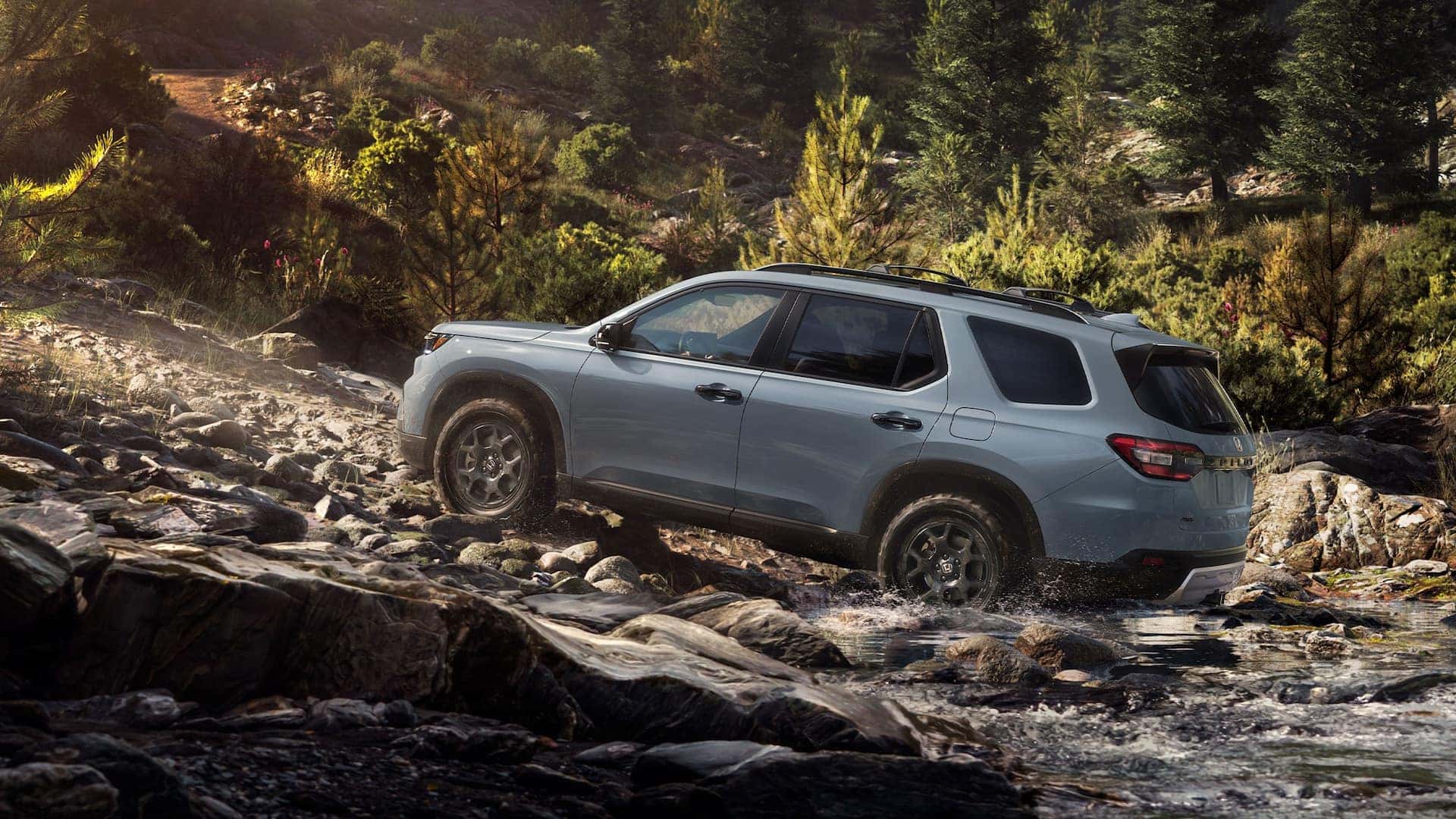 A light blue Honda Pilot driving up a rocky creek