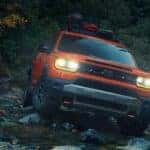 An orange Honda Passport driving over rocky terrain and a creek in a forest