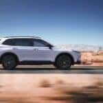 A silver Honda CR-V Hybrid in profile driving down the road in a desert.